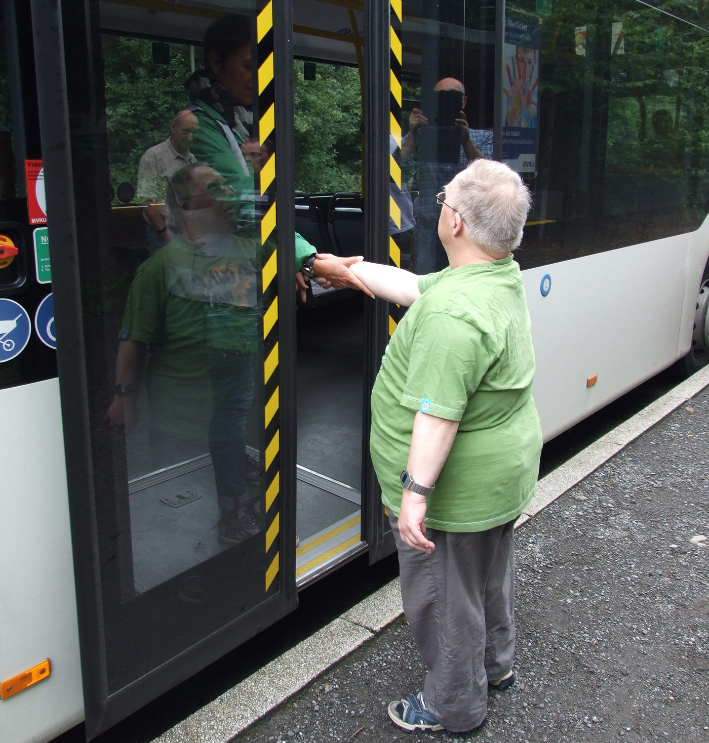 Ein Mann steht vor dem Bus und schüttelt einer Frau im Bus die Hand.
