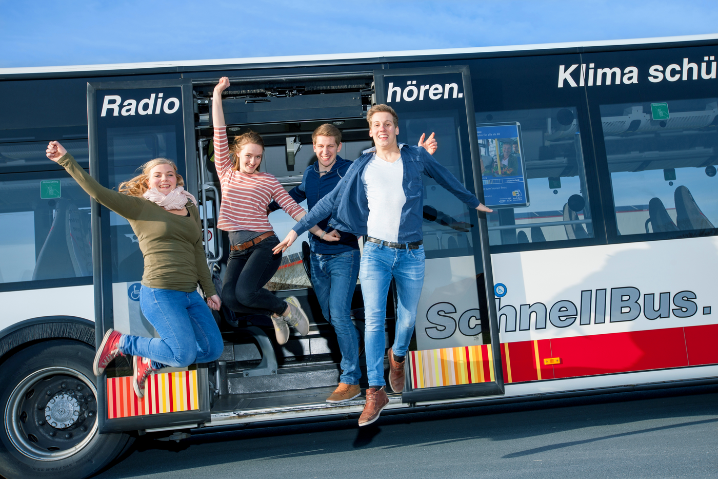 Junge Menschen springen fröhlich aus einem stehenden Bus.